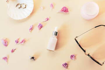 Face serum and women's accessories with dry peony petals on beige background. Top view, flat lay