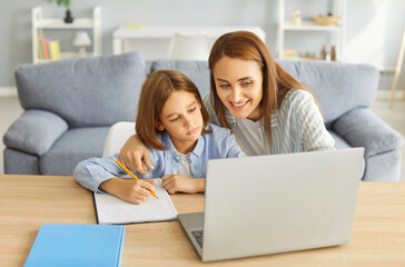 Fototapeta premium Mother and small school pupil learning at home, little teen child boy busy doing lessons, smart kid schoolboy studying remotely online near laptop, writing in copybook, mentor teacher helping 