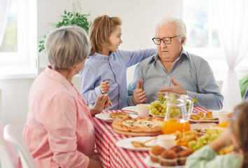 Grandfather and little child boy talking while sitting at a dinner table full of homemade food together with grandma and other family members. Family, grandparents, young and old generation concept