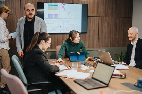Team members collaborating during a business meeting in a modern office, analyzing charts and exchanging ideas, fostering strategic planning and creativity in a professional work environment.