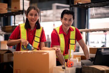 Factory Worker Team Sealing Boxes for Shipment in Warehouse with Smiles and Wearing Safety Vests...