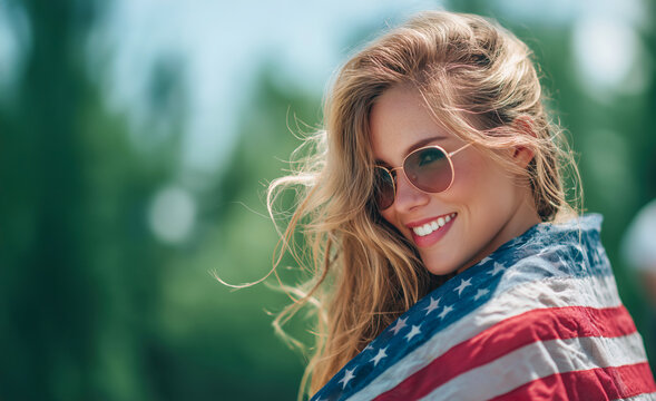 Woman wrapped in American flag enjoying sunny day outdoors at a festive gathering with bright smile and sunglasses - Powered by Adobe