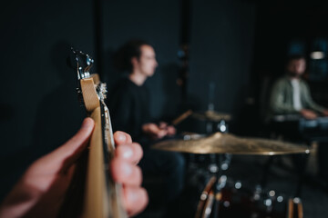 Focused view of a guitar being played with blurred musicians in the background, capturing the...