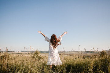 Young woman feeling free raising arms in a field at sunset