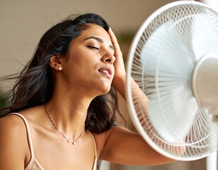A person in front of a fan with an expression of feeling hot, trying to cool down a bit during the summer. Temperature, cool down, air, scorching