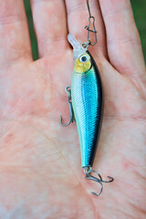 Wobbler in the hand of a fisherman on the background of a spinning reel. Fishing tackle. Selective focus