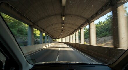 Obraz premium Car windshield view driving through concrete tunnel with arched ceiling and support columns. Highway underpass infrastructure transportation. Urban road travel concept banner horizontal