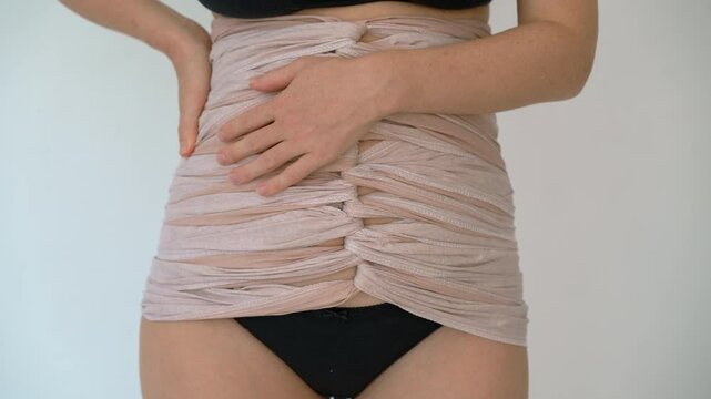 Close-up of postpartum woman's belly wrapped in traditional bengkung belly binding cloth, symbolizing healing and support after childbirth in natural way.