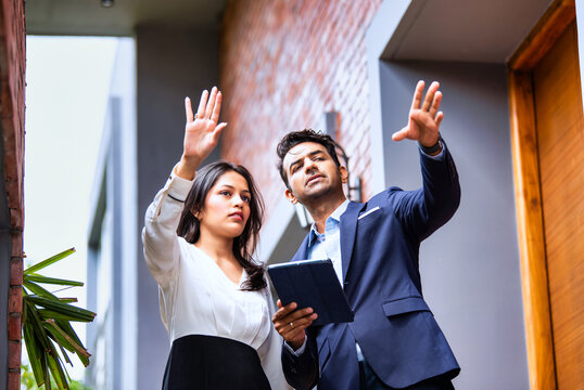 Indian coworkers in formalwear consult outdoors with tablet and coffee, standing near modern office