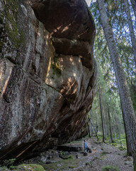 A man standing at the base of a massive rock formation known as Pirunkirkko (Devil’s Church) in Paistjärvi, Finland. This stunning geological site lies deep in the forest, with textured stone surfaces