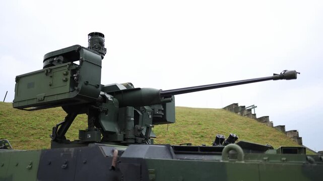 Armored vehicle turret with long barrel automatic cannon stands ready on grassy hill under overcast sky showcasing modern military tech and battlefield readiness in static defensive position
