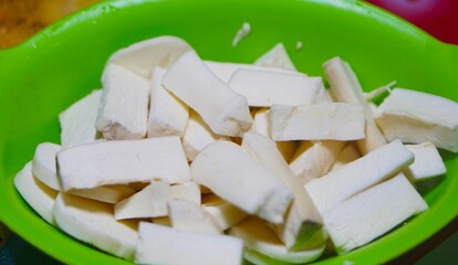 Freshly peeled cassava slices in a green bowl, ready to cook, prepared for a traditional Southeast Asian dish.