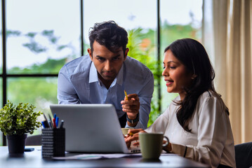 Indian businessmen Working on laptop and reviewing project papers together at desk in indoor office