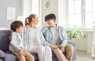 Happy mother spending leisure time with sons, engaging in conversation on the sofa at home. Close...