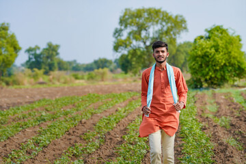 young indian farmer standing at green agricultural field