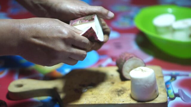 A man's hands cut and peel cassava using a survival knife, which looks clean and white.