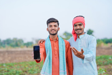 two young indian farmer holding smartphone together at agricultural field