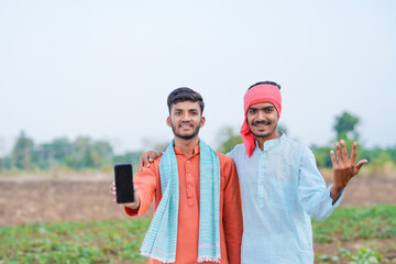 two young indian farmer holding smartphone together at agricultural field