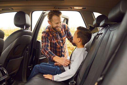 Happy father helps child with safety belt in backseat of his modern car. Smiling adult man checks if son remembers to buckle up before summer or autumn road trip vacation holiday weekend together