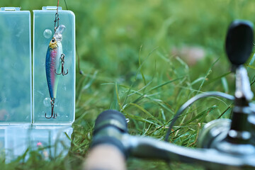 Wobbler with a box for accessories on the background of a spinning reel. Fishing tackle. Selective focus.