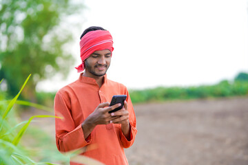 young indian farmer using smartphone standing at agricultural field