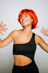 Woman with bright orange hair expressing joy in a stylish black outfit during a studio shoot