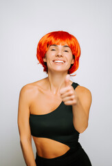 Smiling woman with orange wig giving a thumbs-up gesture in a studio setting