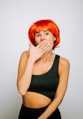 Woman in black outfit expresses surprise with red wig in a plain background
