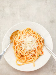 Bucatini pasta with tomato sauce, grated cheese and basil resting on a white plate with cutlery