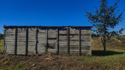 Old abandoned wooden train wagon in a field with blue sky