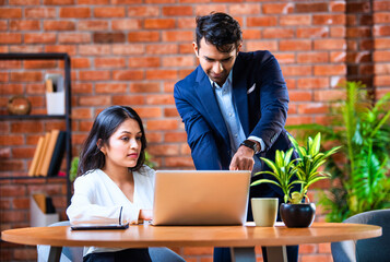 Indian businessmen Working on laptop and reviewing project papers together at desk in indoor office