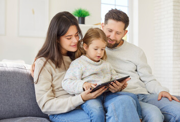 Positive parents and daughter spend online leisure time using a tablet PC at home. Digital activity...