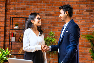 Indian professionals finalize deal with handshake, smiling after discussion in modern office