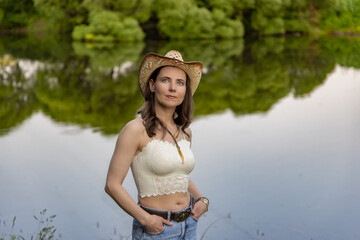 a young woman in a straw hat and lace top, standing against the background of nature. She wears a...