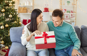 Husband and wife open gift boxes together at home, celebrating New Year or Christmas. Their...