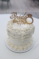 White bridal shower cake with Bride to Be topper and elegant floral icing decorations. Perfect for...