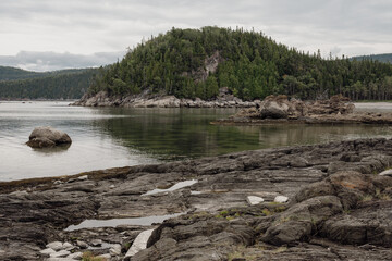 view from the rocky beach of a lake shore with a calm lake under a cloudy sky in summer with a hill...