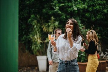 A cheerful woman holding a colorful drink, celebrating and enjoying outdoor party ambiance.