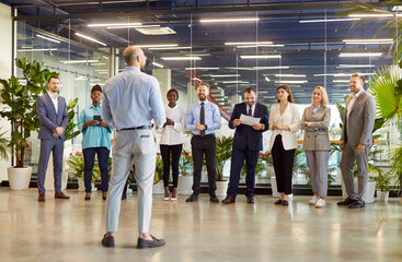 Back view of business leader or coach standing in front of diverse group of company employees. Multinational male and female team on business meeting or training standing in row, listening to speaker.