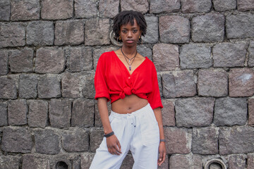 sexy black girl with red sweater and white pants modeling on a street wall