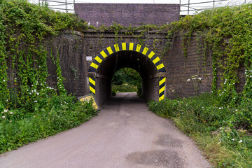 Narrow road passing under a low bridge with hazard stripes