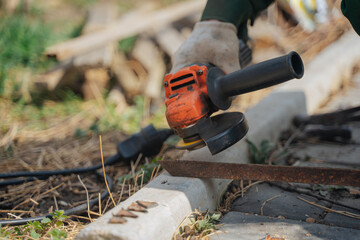 A man cuts off a piece of metal with a grinder. The power tool is in the hands of the master. Construction works.