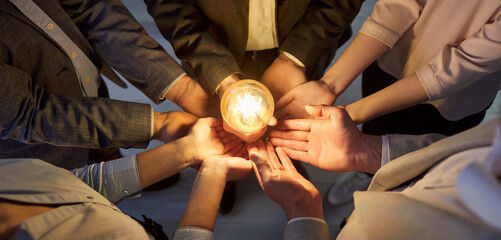 Group of company employees standing in circle, joining hands and holding glowing light bulb....