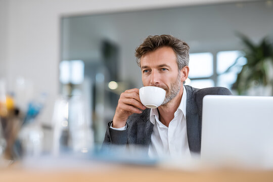 A handsome man drinking coffee in an office, sitting at a desk