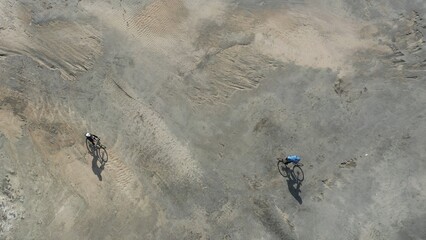 Aerial view of man and woman on bikes riding through the desert on a bright sunny day.