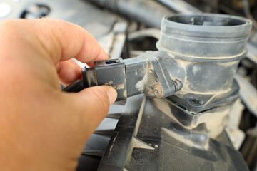A mechanic disconnects an automotive mass airflow sensor, likely during engine diagnostics or repair. This common maintenance procedure helps ensure optimal vehicle performance.