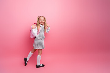 Young schoolgirl in uniform smiling confidently on pink background with backpack preparing for a new academic year