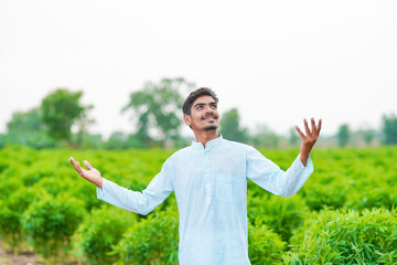 young indian farmer standing at green agricultural field