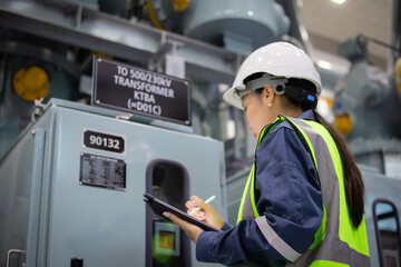 Engineer inspects gas insulated switchgear equipment carefully while taking notes on digital tablet...