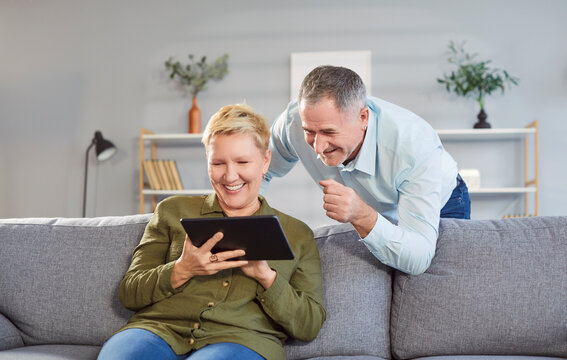Happy Caucasian senior elderly couple grandparents using tablet together,surfing social media, e-banking, e-commerce or having online shopping on application sitting on sofa in living room at home.